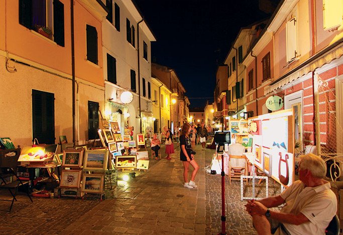 Evening market in the old town of Cesenatico, with paintings on display along the street